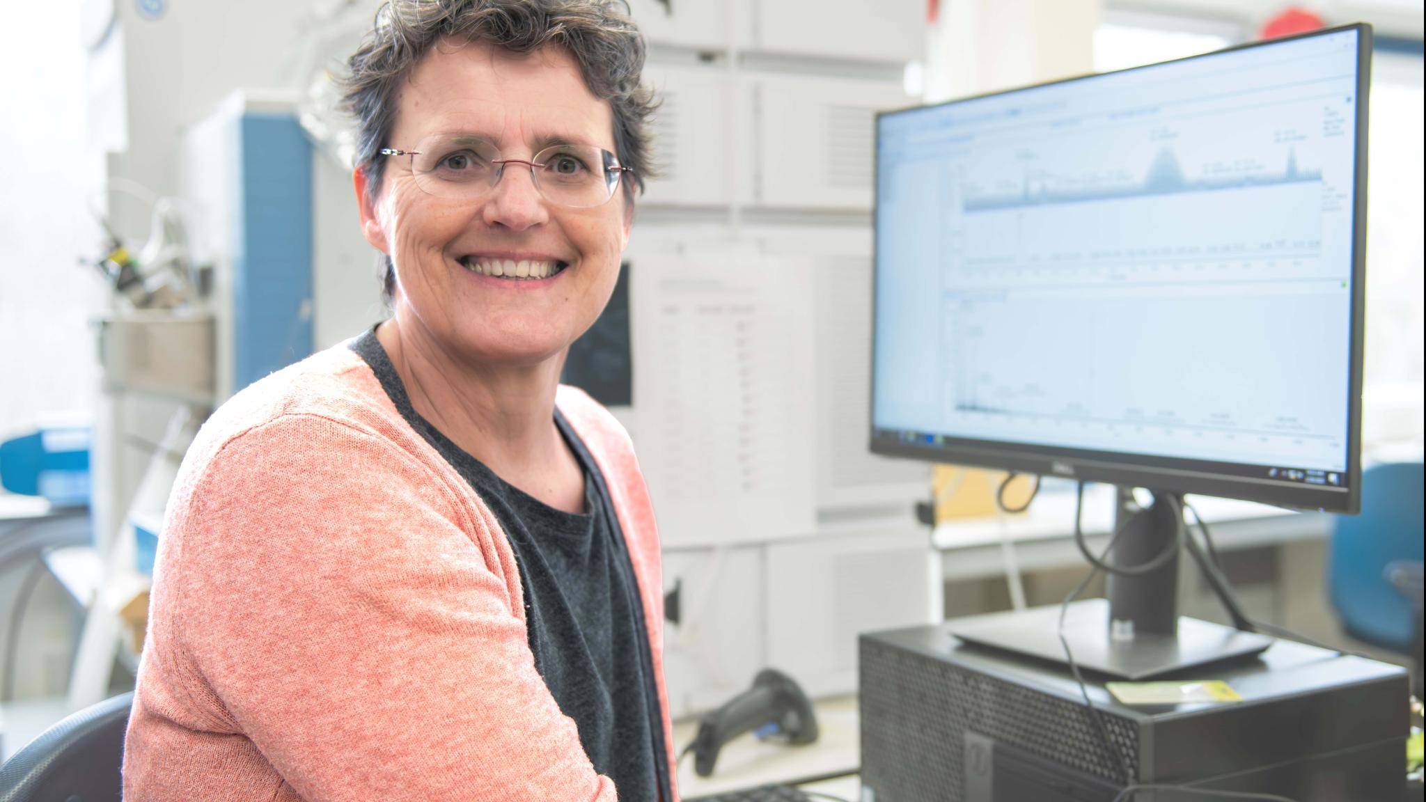 A woman sitting in front of a computer, looking in the camera smiling