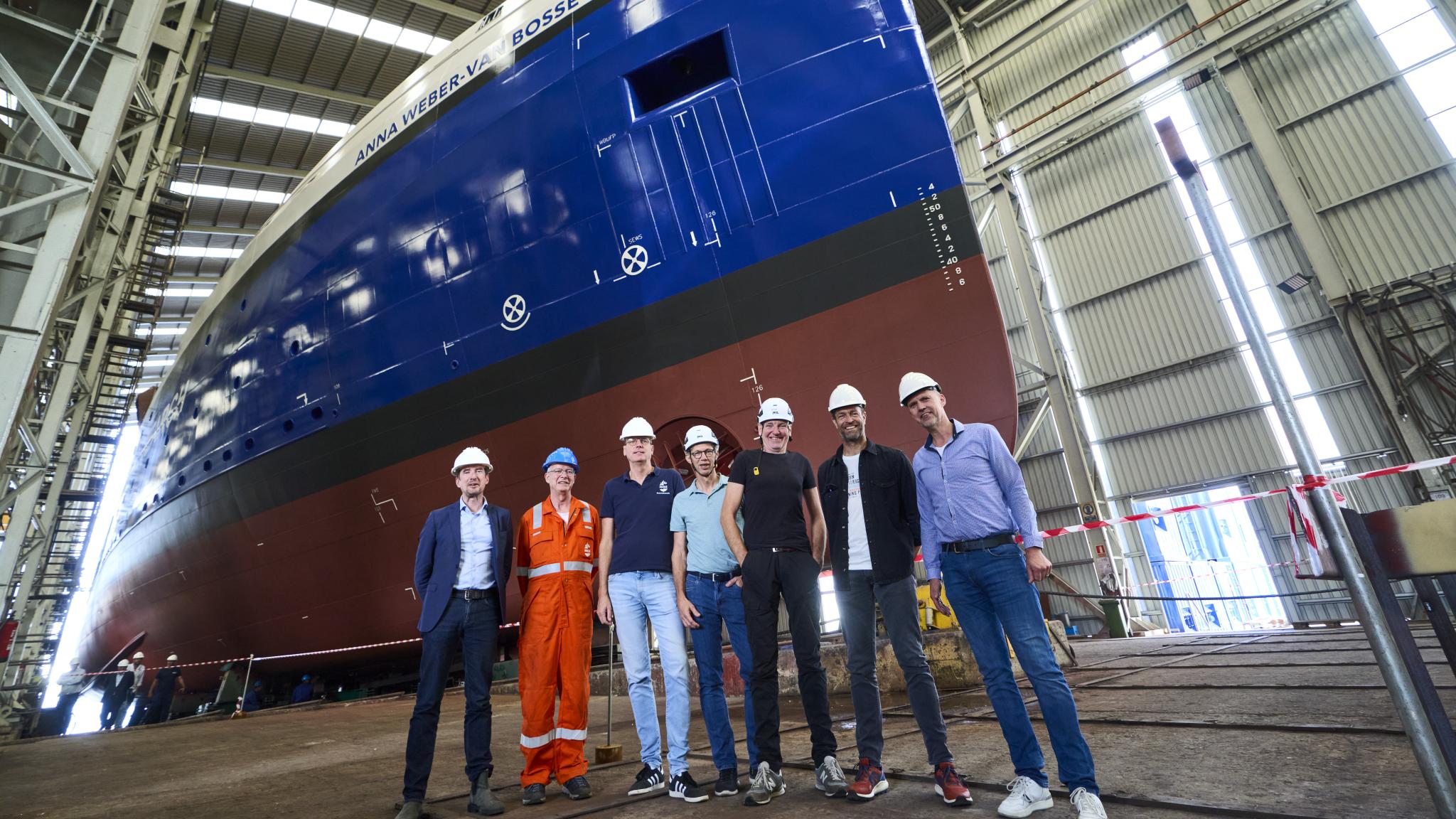 Zeven personen poseren voor een blauw schip