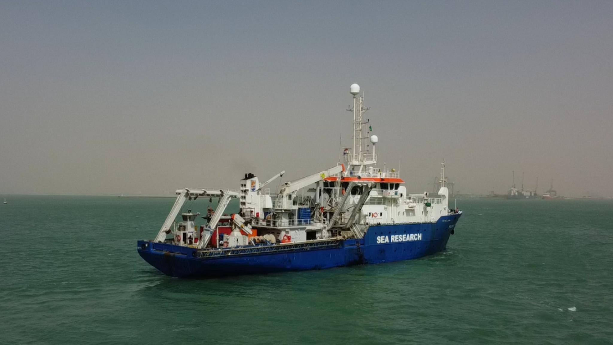 A blue-and-white research vessel labeled “SEA RESEARCH” sailing on calm green water.