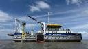 A research vessel installs a yellow pole in shallow water using a crane on deck.