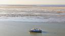 Luchtfoto van een onderzoeksschip dat langs de droogvallende wadplaten van de Waddenzee vaart