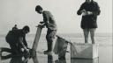 Three researchers on a mudflat. Two are using a spigot to tak a sample of the sediment, one is taking notes.