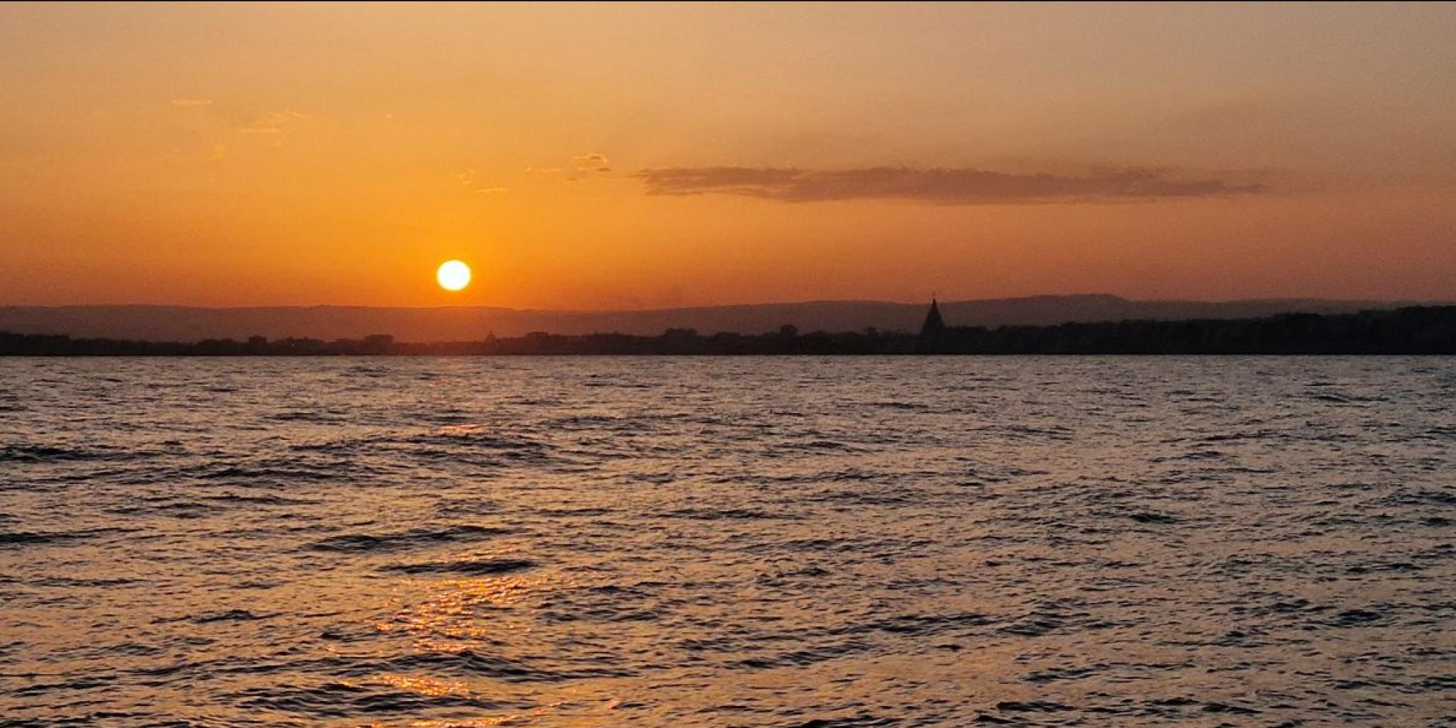 Sicily seen from the vessel, with an orange coloured sunset sky due to all the dust in the sky