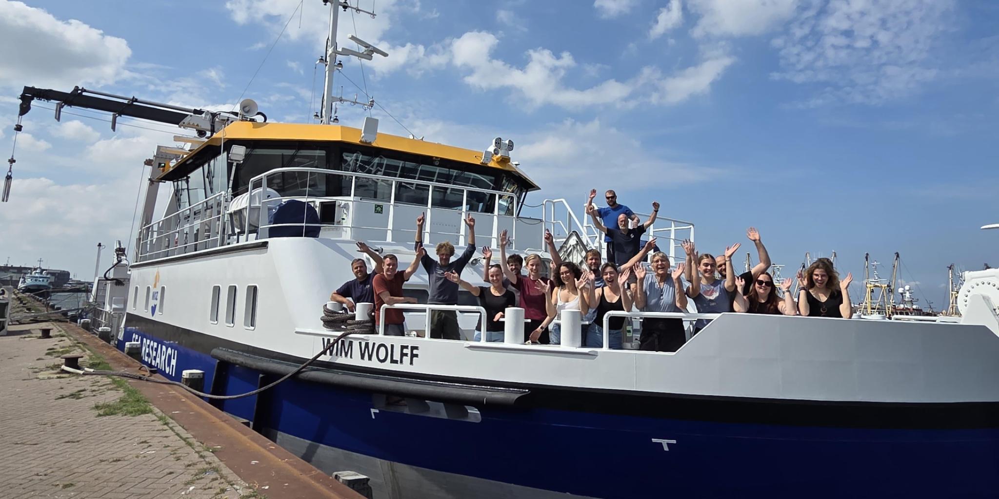 A group of people standing on the front deck of the RV Wim Wolff, cheering enthusiastically