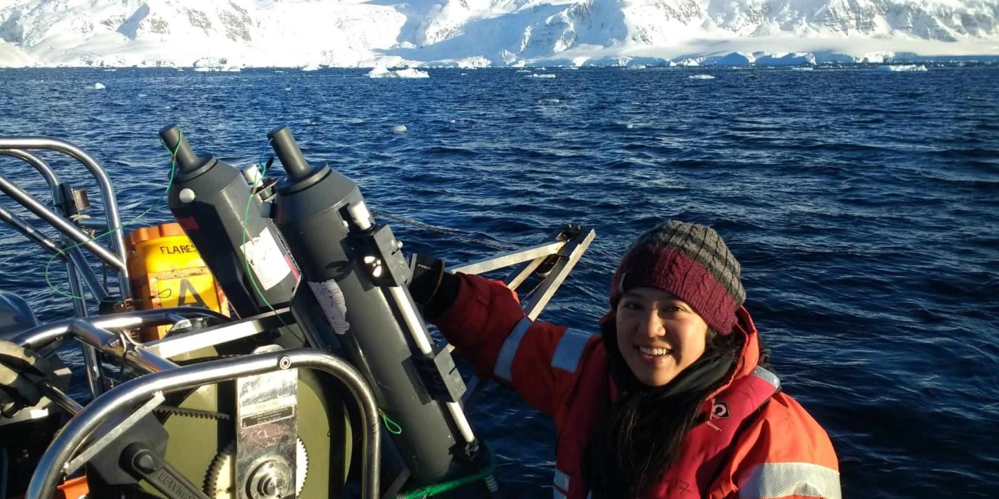 emale researcher on board a boat in Ryder Bay, west Antarctic Peninsula, with snow-covered mountains in the background.