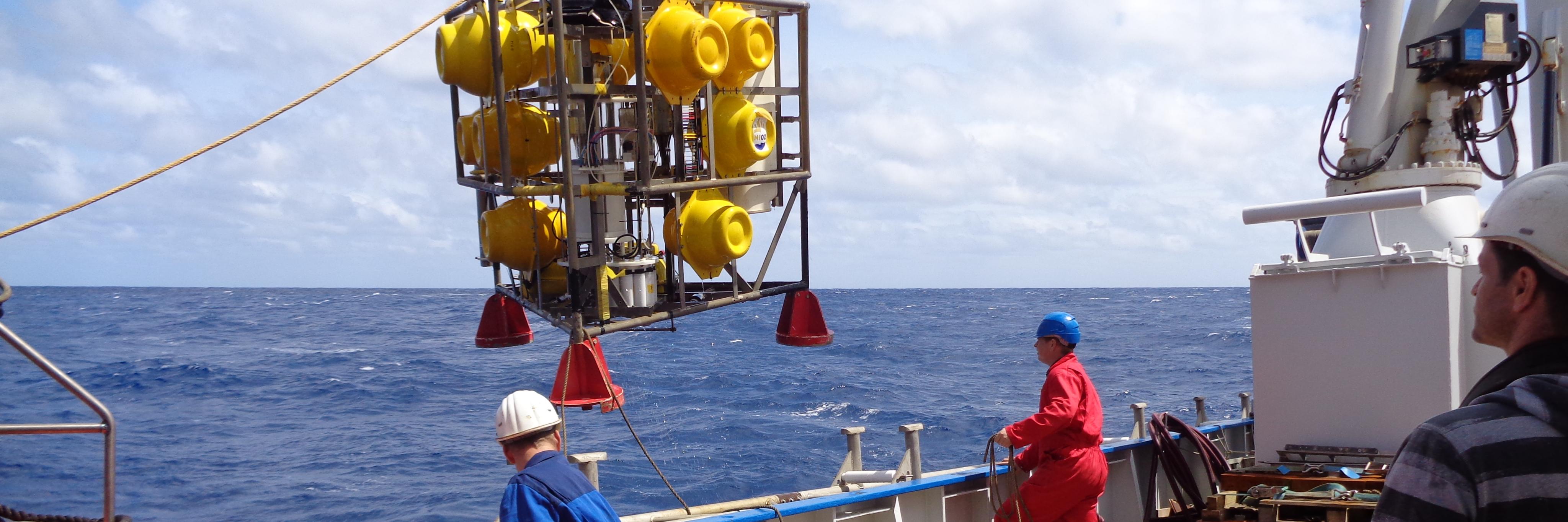 Twee bemanningsleden helpen bij het binnenhalen van een geel onderzoeksapparaat op het onderzoeksschip Pelagia.