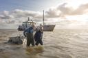 Two NIOZ researchers wading through the water pulling a floating cart. Ship in the background.